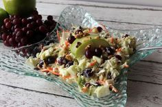 a glass bowl filled with fruit and veggies next to grapes on a wooden table