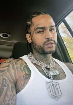 a man with tattoos sitting in the back seat of a car wearing a white tank top