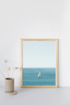 a white vase sitting next to a framed photo on top of a table with a sailboat in the distance