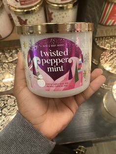 a hand holding up a candle that says twisted pepper mint in front of other candles