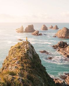 a person standing on the edge of a cliff overlooking the ocean with rocks in the background