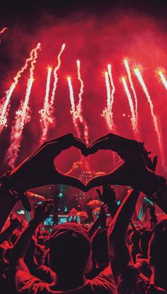 people holding up their hands in the shape of a heart as fireworks go off behind them