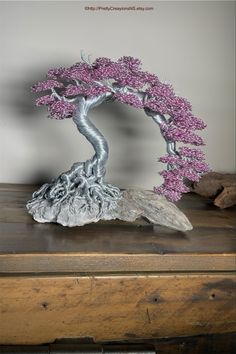 a bonsai tree with pink flowers growing out of it's roots on top of a wooden table