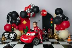 a boy is sitting in a toy car surrounded by balloons