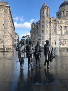 three statues of men walking down a wet sidewalk in front of large buildings with dome tops