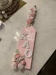 a pink sign that says kao with flowers on it sitting on top of a counter