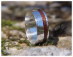 a silver ring with red wood inlays on top of a rocky surface,