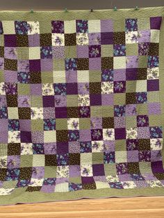 a purple and green quilt hanging on a wall