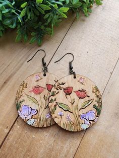 two wooden earrings with flowers painted on them sitting on a wood floor next to plants