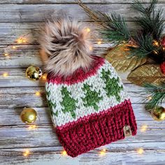 a red and white knitted hat next to christmas decorations on a wooden table with lights