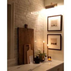 candles are lit on a white counter in front of two pictures and a cutting board