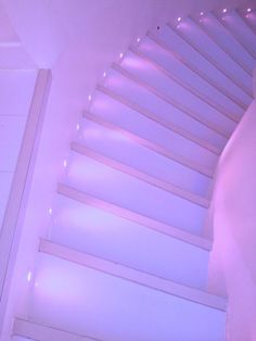 a bed sitting under a purple light next to a white wall and ceiling with lights on it