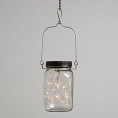 a glass jar filled with white lights hanging from a metal hook on a gray wall