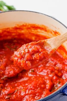 a wooden spoon full of marinara sauce in a blue pot with parsley on the side