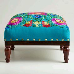 a foot stool with colorful flowers on the top and legs, sitting in front of a white background