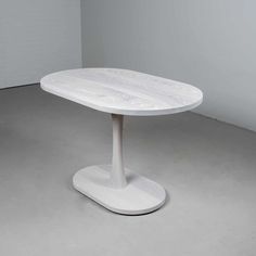 a white round table with an oval base in the middle, on a concrete floor