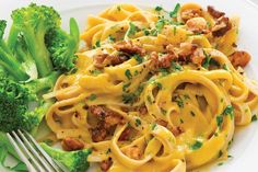 a white plate topped with pasta and broccoli next to a fork on a table