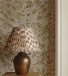 a lamp sitting on top of a wooden table next to a wallpapered wall