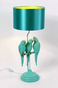 three green birds sitting on top of a table next to a blue lampshade