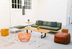 an outdoor patio with two chairs, a couch and a coffee table in front of a white building