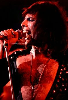 a man with long hair and piercings on his chest holding a microphone in front of him