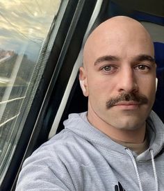 a bald man with a goatee and mustache sitting in a bus looking at the camera