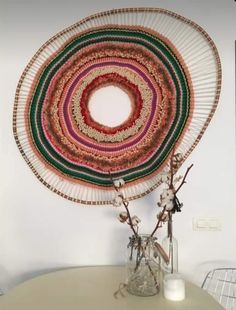 a white table topped with a vase filled with flowers next to a round wall hanging