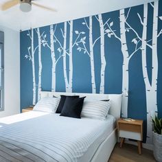 a bedroom with blue walls and white trees painted on the wall behind the headboard