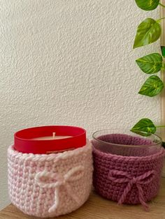 two crocheted containers with a red candle in one and a pink container on the other