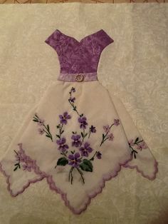 a dress with purple flowers on it sitting on top of a white tablecloth next to a wall