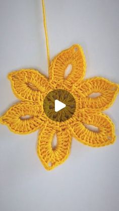 a crocheted yellow flower ornament hanging on a white wall with a video play button