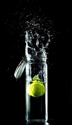 a tennis ball in a glass jar with water splashing on it