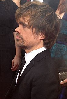 a man in a black suit and tie at an event with other people around him