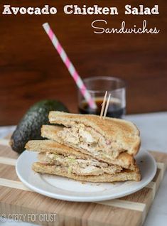 a sandwich cut in half sitting on top of a white plate next to an avocado