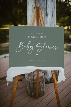 a welcome sign for a baby shower is displayed on an easel in front of a tree