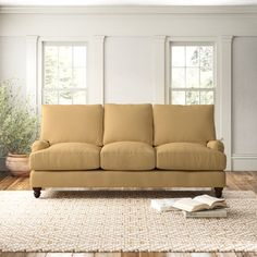 a living room scene with focus on the couch and book lying on the floor in front of the window