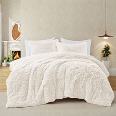 a bed with white comforter and pillows in a room next to a fire place