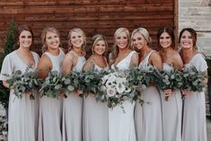 a group of women standing next to each other in front of a wooden wall holding bouquets