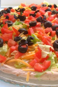 a pizza topped with lettuce, tomatoes and olives on a glass platter