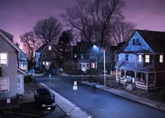 an empty street at night with some houses in the background and one car parked on the side