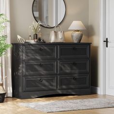 a black dresser sitting in front of a mirror on top of a wooden floor next to a potted plant