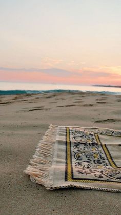 a blanket is laying on the beach at sunset