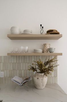 two open shelves above a kitchen counter with plates and bowls on it, one shelf holding a book