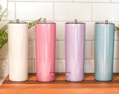 three different colored tumbles sitting on top of a wooden counter next to a potted plant