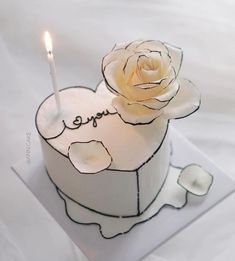 a white cake with a single candle on it and the word love spelled in cursive writing