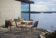 an outdoor table and chairs with water in the backgrouds behind it on graveled area next to stone wall