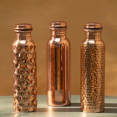 three copper colored vases sitting next to each other on top of a blue table