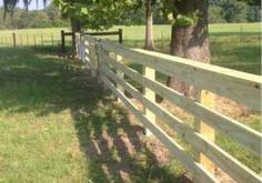 a wooden fence in the middle of a grassy field next to a tree and some trees