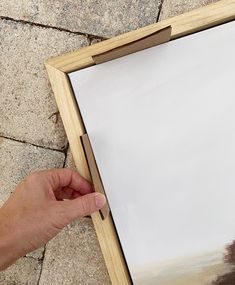 a person is holding a piece of wood near a painting on the ground with their hand