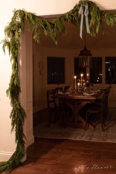 the table is set for dinner with candles and greenery on it, along with other decorations